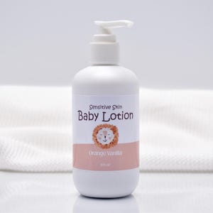 Op de afbeelding: Een witte baby lotion fles met een pompdosser. Het etiket leest "Sensitive Skin Baby Lotion" met een leeuwen illustratie en "Orange Vanilla". De fles bevat 237 ml lotion.