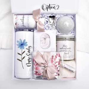 May include: A white gift box labeled Option 2 containing a white tumbler with a blue flower and the text Nurse Emily, a lotion bottle, a heart-shaped spoon, a bath bomb, a candle with text, a small boxed item, a lip balm, and a pink ribbon.