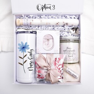 May include: A white gift box labeled Option 3 containing a white tumbler with a blue flower and the text Nurse Emily, a glass tube of bath salts, a silver spoon, a small jewelry box, a candle, a lip balm, and a gift bag with a pink ribbon.