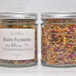 May include: Two glass jars filled with a blend of dried flowers, including rose petals, hibiscus, chamomile, and calendula. The jars have silver lids and are labelled "Bath Flowers rose hibiscus".