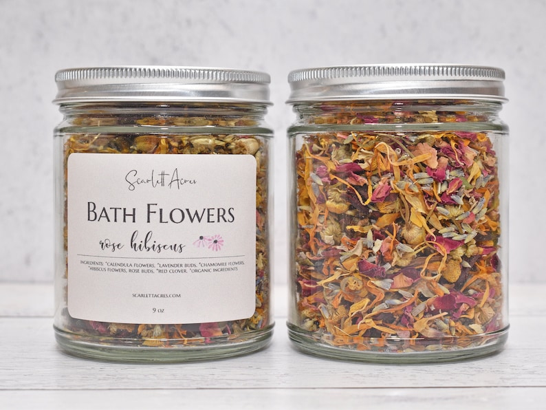 May include: Two glass jars filled with a blend of dried flowers, including rose petals, hibiscus, chamomile, and calendula. The jars have silver lids and are labelled "Bath Flowers rose hibiscus".