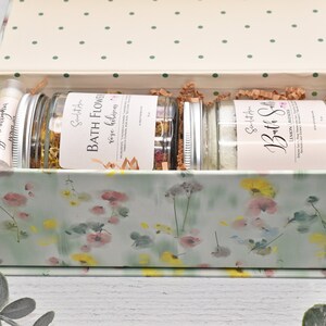 May include: A floral patterned gift box with a lid open, revealing three glass jars filled with bath products. The jars are labelled "Bath Flower, Rose Hibiscus" and "Bath Salt, Lemon Lavender".