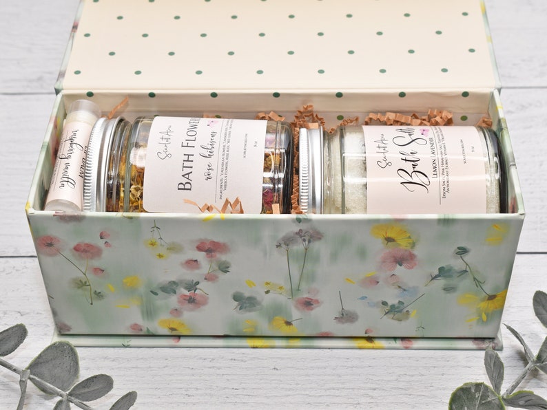 May include: A floral patterned gift box with a lid open, revealing three glass jars filled with bath products. The jars are labelled "Bath Flower, Rose Hibiscus" and "Bath Salt, Lemon Lavender".