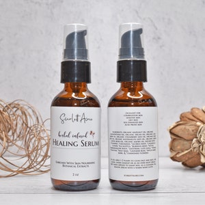 May include: Two amber glass bottles with black pump tops filled with a herbal infused healing serum. The bottles are labeled "Scarlett Acru" and "herbal infused HEALING SERUM". The bottle on the right has a list of ingredients and instructions for use.