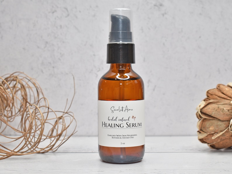 May include: A brown glass bottle with a black pump top and a white label that reads "Scarlet Acres Herbal Infused Healing Serum" with a small floral design. The bottle is 2 oz and enriched with skin nourishing botanical infused oils.
