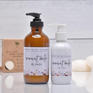 May include: Two bottles of cream facial cleanser with the words "coconut milk & oats" on the labels. One bottle is amber, the other white. A box of hemp cotton rounds and two white soap bars are also visible.