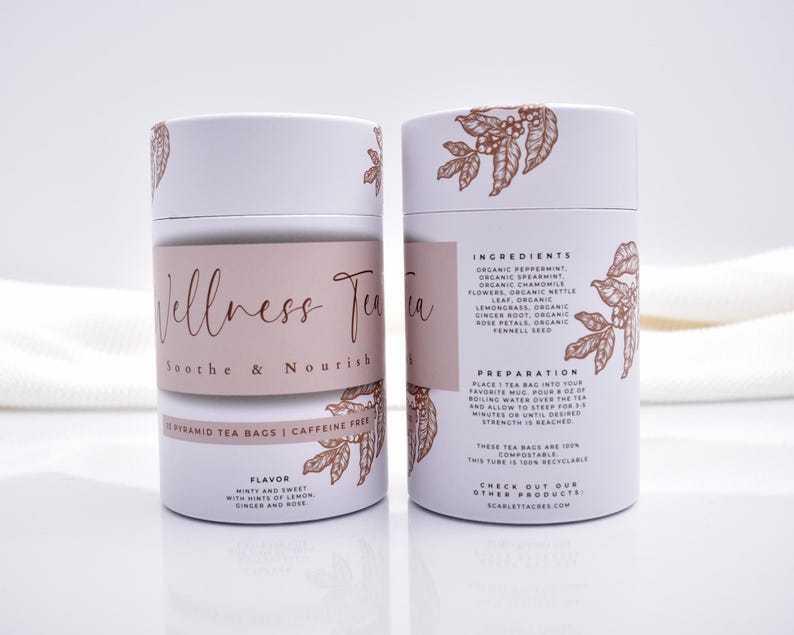 May include: Two cylindrical white cardboard tea canisters featuring copper-colored botanical illustrations. The front label reads Wellness Tea Soothe & Nourish, while the back lists ingredients including peppermint, spearmint, chamomile, and ginger.