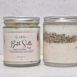 May include: Two glass jars with silver lids filled with bath salts. The jar on the left has a label that reads "Scarlett Acre Bath Salts Lemon Lavender Epsom Salt, Pink Himalayan Salt, Essential Oils, Rosemary Antioxidant Extract, Vitamin E, Organic Ingredients ScarlettAcres.com 9 oz."