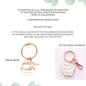 May include: Two rose gold-toned metal keychains. One features a bear silhouette with the text 'Mama Bear' and the other is a scalloped-edge charm with the text 'Mama, you got this!' and a lobster clasp. The image includes text about donations.
