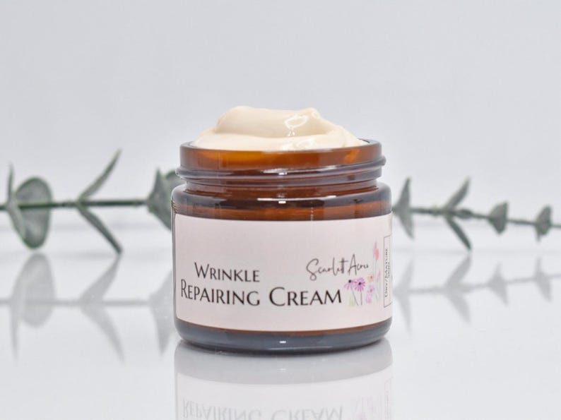 May include: A brown glass jar with a white label that reads "Wrinkle Repairing Cream" and "Scarlet Ann" in a pink floral design. The jar is filled with a white cream.