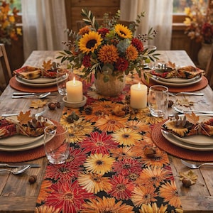 May include: A table runner featuring a vibrant floral pattern of sunflowers and dahlias in shades of orange, red, and yellow on a black background, centered on a wooden table with place settings, candles, and a floral centerpiece.