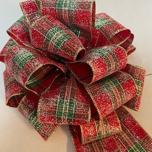 May include: A large, decorative bow made of red, green, and gold plaid ribbon. The ribbon has a glittery finish, adding sparkle. The bow is likely for holiday or gift decoration.