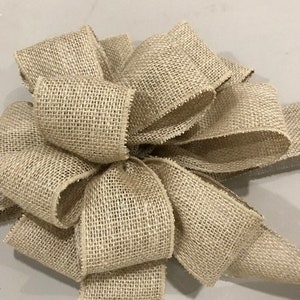 May include: A large, rustic burlap bow with a natural beige color. The bow is made of multiple layers of burlap ribbon, creating a full and textured look.
