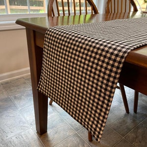 May include: Black and white checkered table runner on a wooden table with two chairs. The table runner is made of a soft, woven fabric.