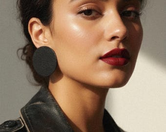 May include: A woman wearing a black leather jacket and large, round black earrings. Her dark hair is pulled back, and she wears dark red lipstick. The image is a close-up, focusing on the face and upper body.
