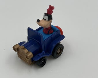 Puede incluir: Un pequeño coche de juguete azul con detalles dorados. El coche presenta un personaje de dibujos animados con cabeza negra, cara color canela y sombrero y camisa rojos. Tiene ruedas negras e interior azul.