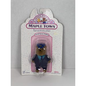 May include: A Maple Town Sheriff Barney Bulldog toy figure in its original packaging. The figure is a brown bulldog wearing a blue uniform and hat. The packaging includes the text "My Favorite Place to Be" and "Maple Town".