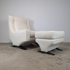 May include: A cream-colored armchair and matching ottoman set. The chair has a high back and curved arms, with a textured, plush fabric. The ottoman is rectangular and sits low to the ground. Both pieces have dark wooden bases.