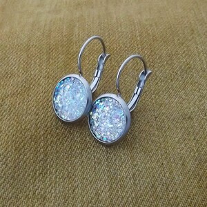 May include: A pair of silver hoop earrings with a round, white glitter-filled charm on each earring.