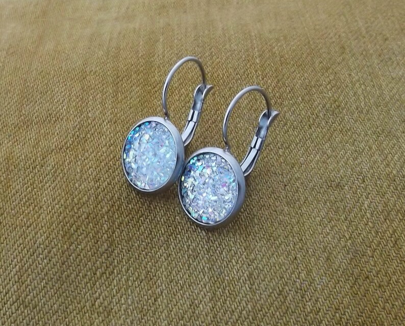 May include: A pair of silver hoop earrings with a round, white glitter-filled charm on each earring.