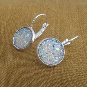 May include: A pair of silver hoop earrings with a round, iridescent glitter design. The glitter is a mix of white, blue, and silver.