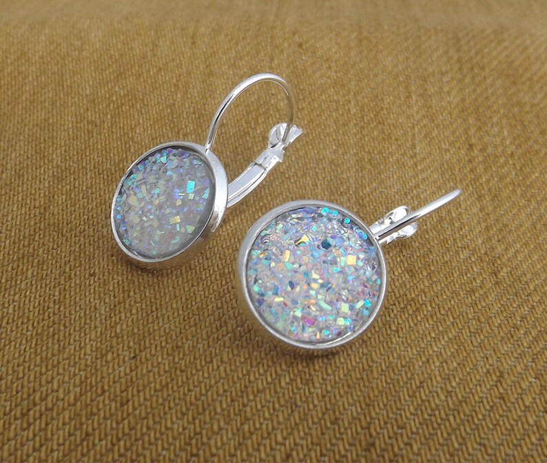 May include: A pair of silver hoop earrings with a round, iridescent glitter design. The glitter is a mix of white, blue, and silver.
