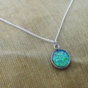 May include: A silver chain necklace with a round pendant featuring a green and blue glitter design.