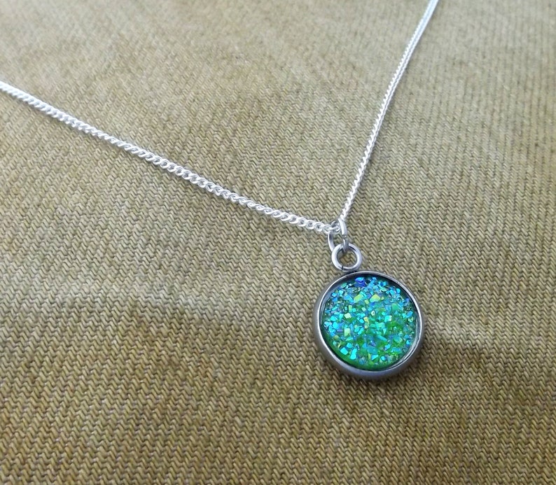 May include: A silver chain necklace with a round pendant featuring a green and blue glitter design.