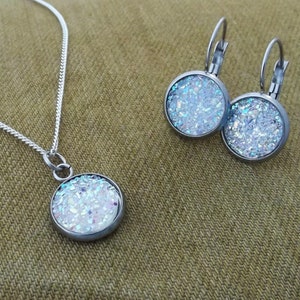 May include: A silver chain necklace and matching earrings with a round pendant and earrings featuring a white glitter design.