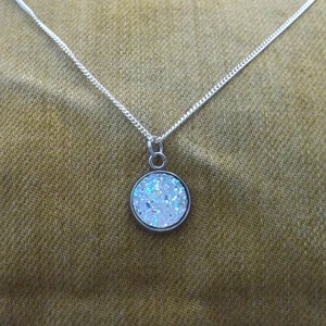 May include: A silver chain necklace with a round pendant featuring a white glitter design.