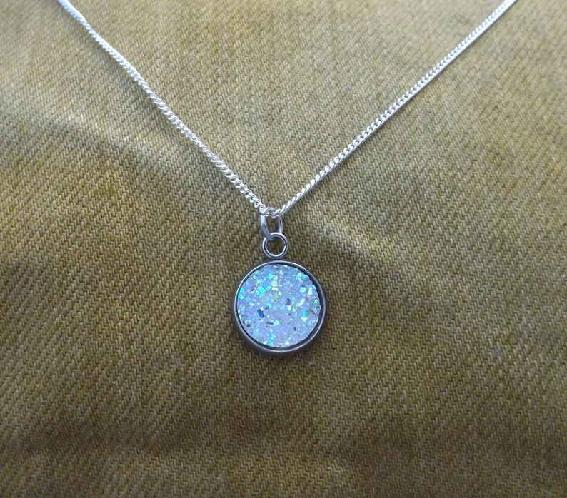 May include: A silver chain necklace with a round pendant featuring a white glitter design.