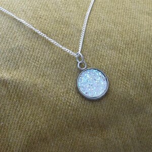 May include: A silver chain necklace with a round pendant featuring iridescent glitter embedded in clear resin.