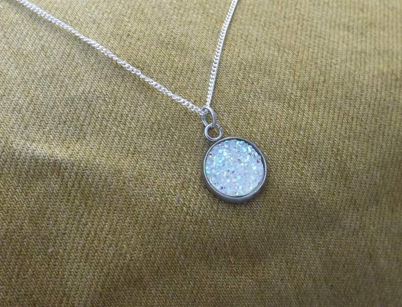 May include: A silver chain necklace with a round pendant featuring iridescent glitter embedded in clear resin.
