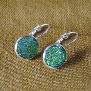 May include: A pair of silver dangle earrings with green glitter round cabochon stones.