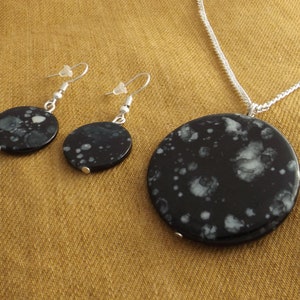 Peut inclure: Un collier avec un pendentif rond en pierre mouchetée noir et blanc et des boucles d'oreilles assorties. Les boucles d'oreilles sont de style pendantes.