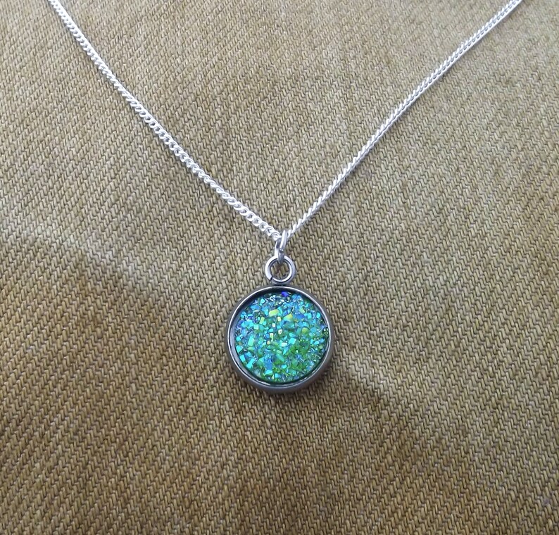 May include: A silver chain necklace with a round pendant featuring a green and blue glitter-filled resin design.
