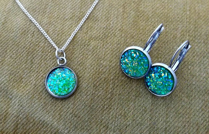 May include: A silver chain necklace with a round pendant featuring green and blue glitter. Matching earrings with the same design are also included.