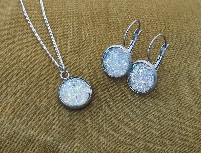 May include: A silver necklace and earrings set with iridescent white glitter round pendants.