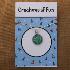 May include: A silver necklace with a green glitter charm on a blue and white card with the text "Creatures of Fun".