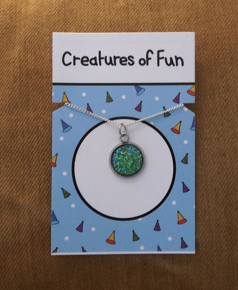 May include: A silver necklace with a green glitter charm on a blue and white card with the text "Creatures of Fun".