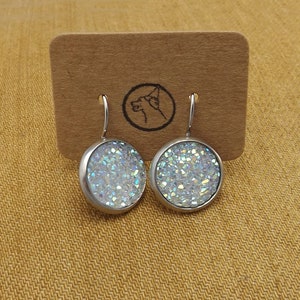 May include: A pair of silver dangle earrings with iridescent white glitter round cabochons.