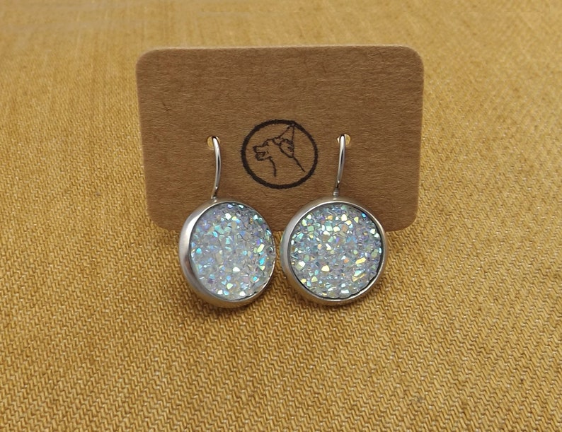 May include: A pair of silver dangle earrings with iridescent white glitter round cabochons.