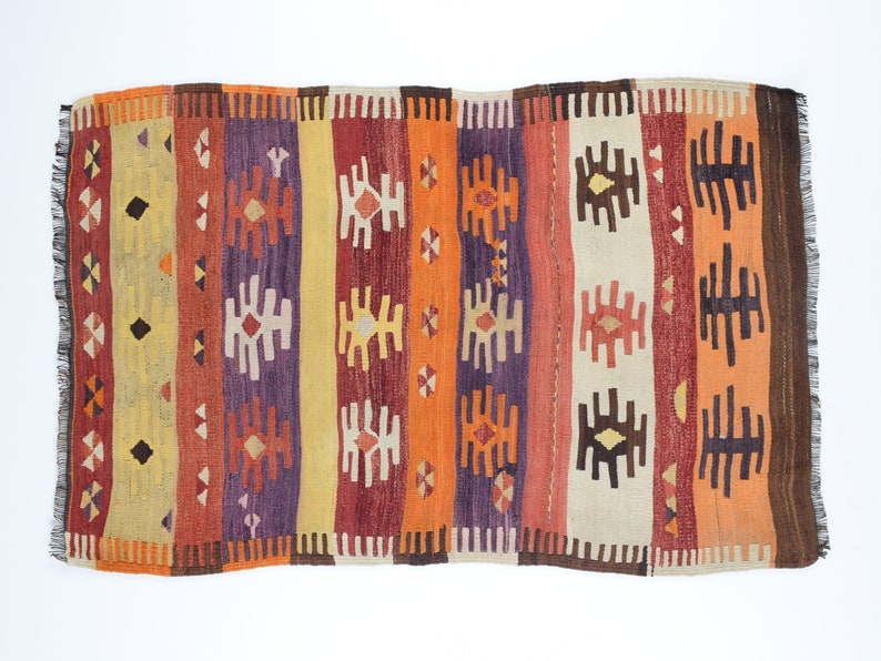 K&ouml;nnte beinhalten: Ein bunter Vintage-Teppich mit einem geometrischen Muster in Rot-, Orange-, Gelb-, Braun- und Violettt&ouml;nen. Der Teppich hat einen Fransenrand und ist mit einem traditionellen Muster gewebt.