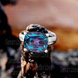 Può includere: Un anello d'argento con una grande pietra rettangolare di colore blu scuro e verde. La pietra preziosa ha una tonalità viola ed è incastonata in una fascia d'argento.