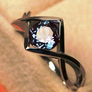 May include: A silver ring with a square setting featuring a round, iridescent blue gemstone. The ring has a twisted band.
