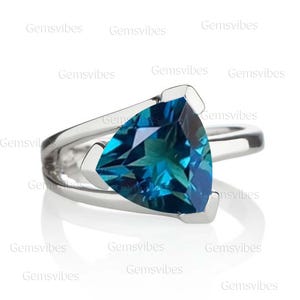 Puede incluir: Un anillo de plata con una piedra preciosa azul triangular. La piedra preciosa tiene un corte facetado y un color azul profundo.