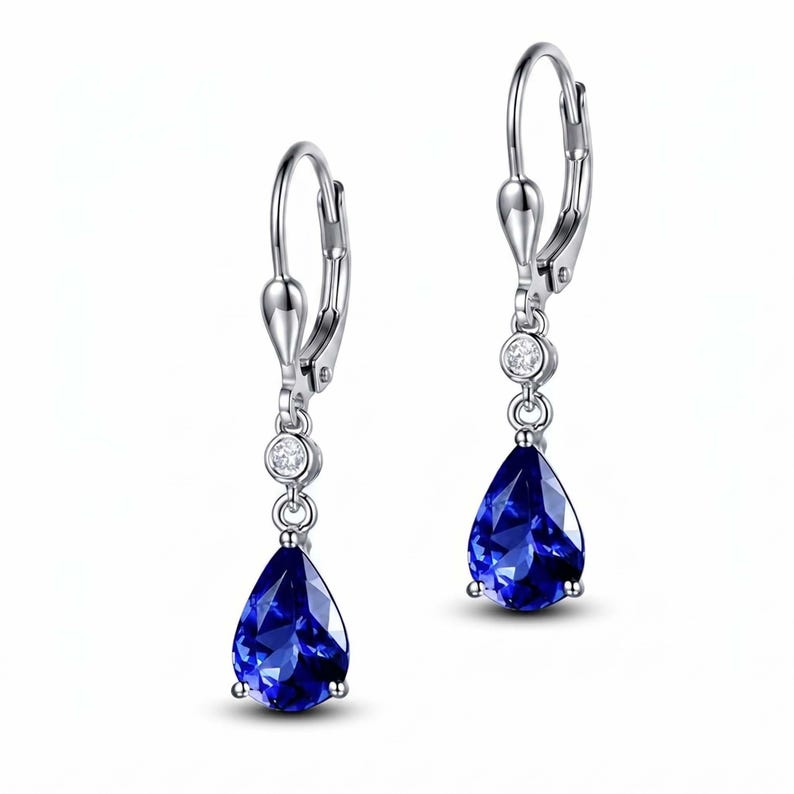 May include: A pair of silver-toned drop earrings. Each earring features a teardrop-shaped, deep blue gemstone suspended below a small, round, clear stone. The earrings have a lever-back closure.