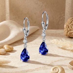 May include: A pair of silver-toned drop earrings. Each earring features a teardrop-shaped, deep blue gemstone suspended below a small, round, clear stone. The earrings have a lever-back closure.