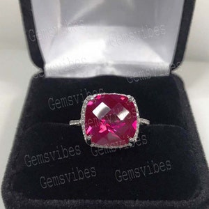 Könnte beinhalten: Nahaufnahme eines Rings mit einem großen, quadratischen, rosafarbenen Edelstein, der von kleineren, weißen Edelsteinen umgeben ist. Der Ring befindet sich in einer schwarzen Samtringbox mit dem Wort "Gemsvibes" auf der Box.