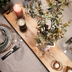 May include: A wooden serving tray with a handle, decorated with candles and greenery. The tray is set on a white tablecloth with two place settings.
